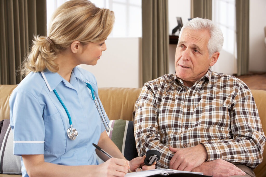 Senior Man Talking To Health Visitor At Home